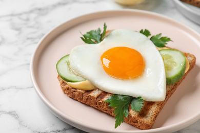 Plate of tasty sandwich with heart shaped fried egg on white marble table, closeup
