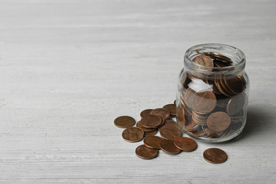 Photo of Glass jar with coins on white wooden table, space for text