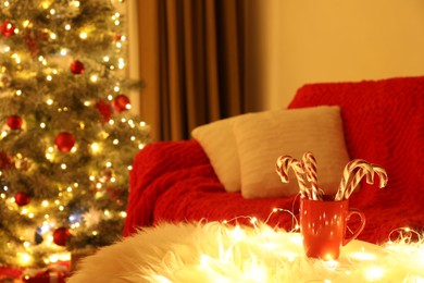 Red cup with candy canes on faux fur in room decorated for Christmas. Interior design