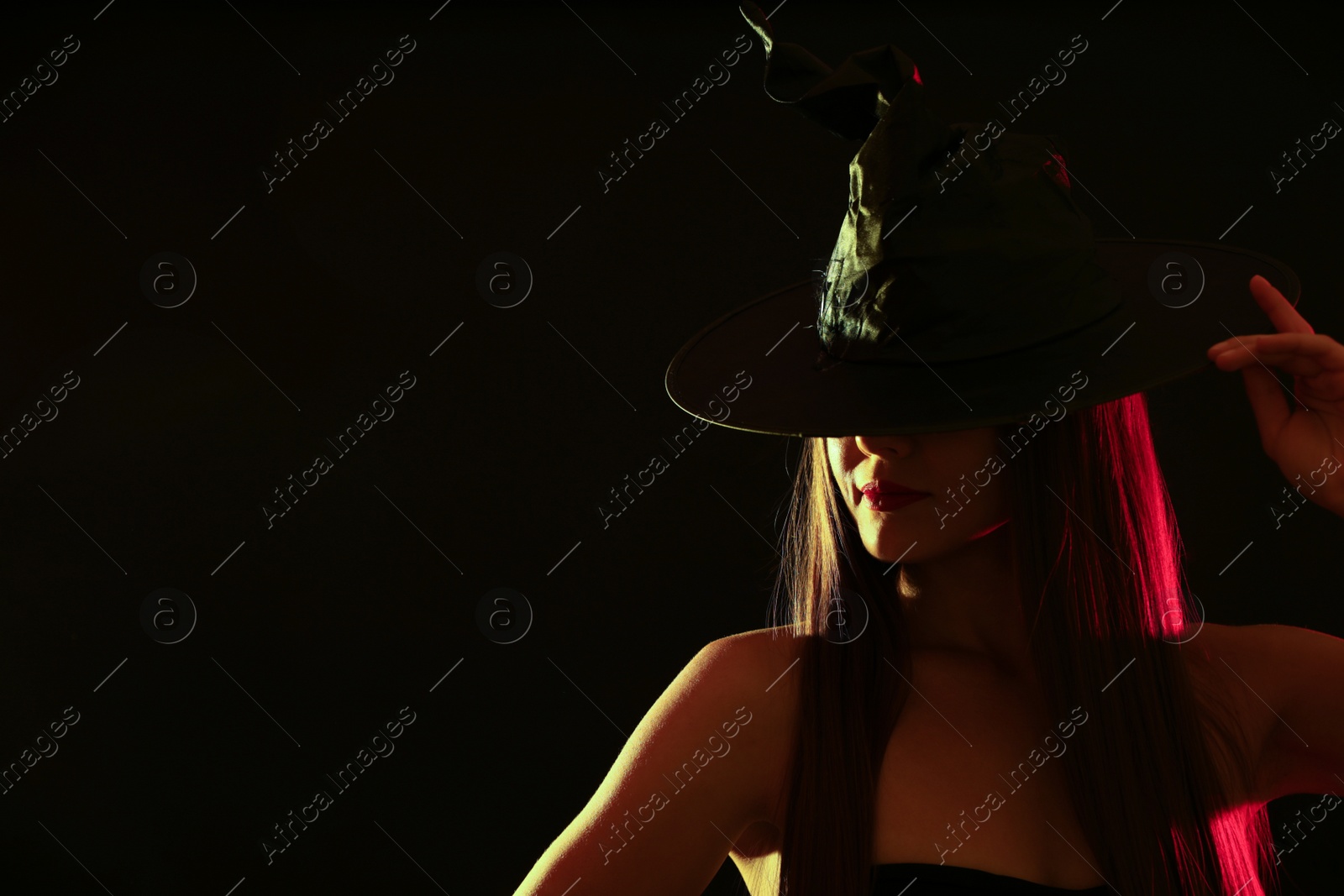 Photo of Young woman wearing witch costume on black background, space for text. Halloween party