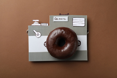 Camera made from donut and piece of cardboard on brown background, top view