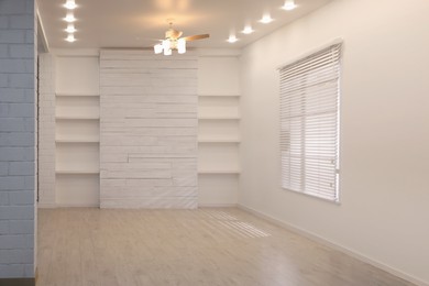 Empty room with textured wall, stylish wooden shelves and large window