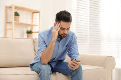 Young man addicted to smartphone on couch at home