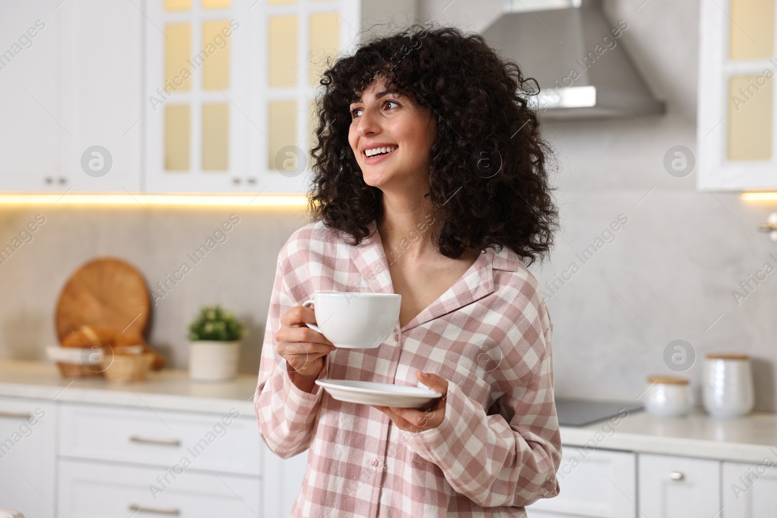 Photo of Beautiful young woman in stylish pyjama with cup of drink in kitchen