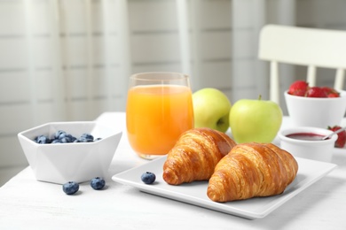 Tasty breakfast with croissants served on white wooden table