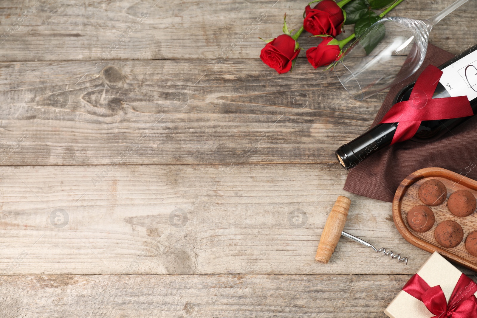 Photo of Bottle of red wine, glass, chocolate truffles, corkscrew, roses and gift box on wooden table, above view. Space for text