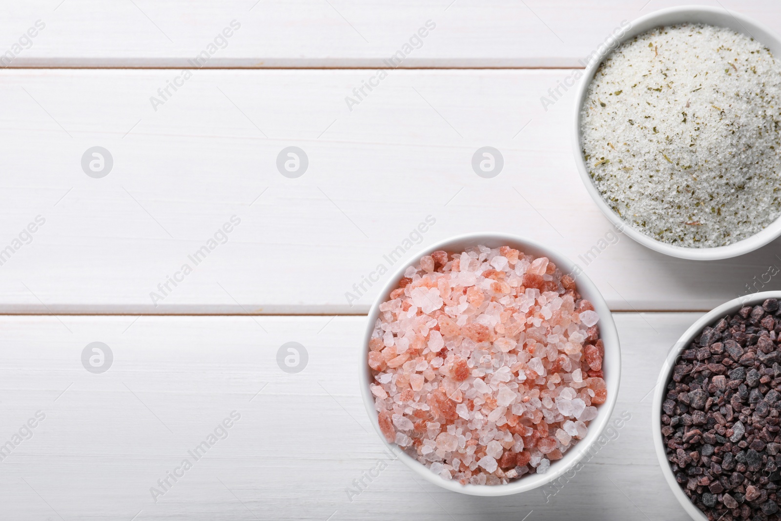 Photo of Different kinds of salt on white wooden table, flat lay. Space for text