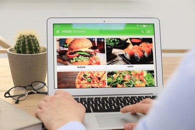 Photo of Man using laptop for ordering food online at table indoors, closeup. Concept of delivery service