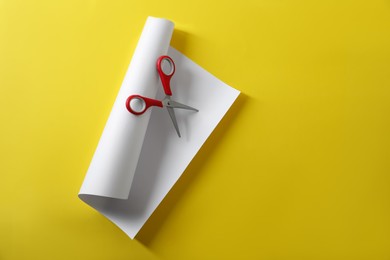 Photo of Red scissors and white paper on yellow background, top view. Space for text