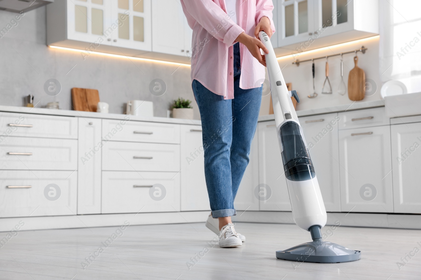 Photo of Woman cleaning floor with steam mop in kitchen at home, closeup