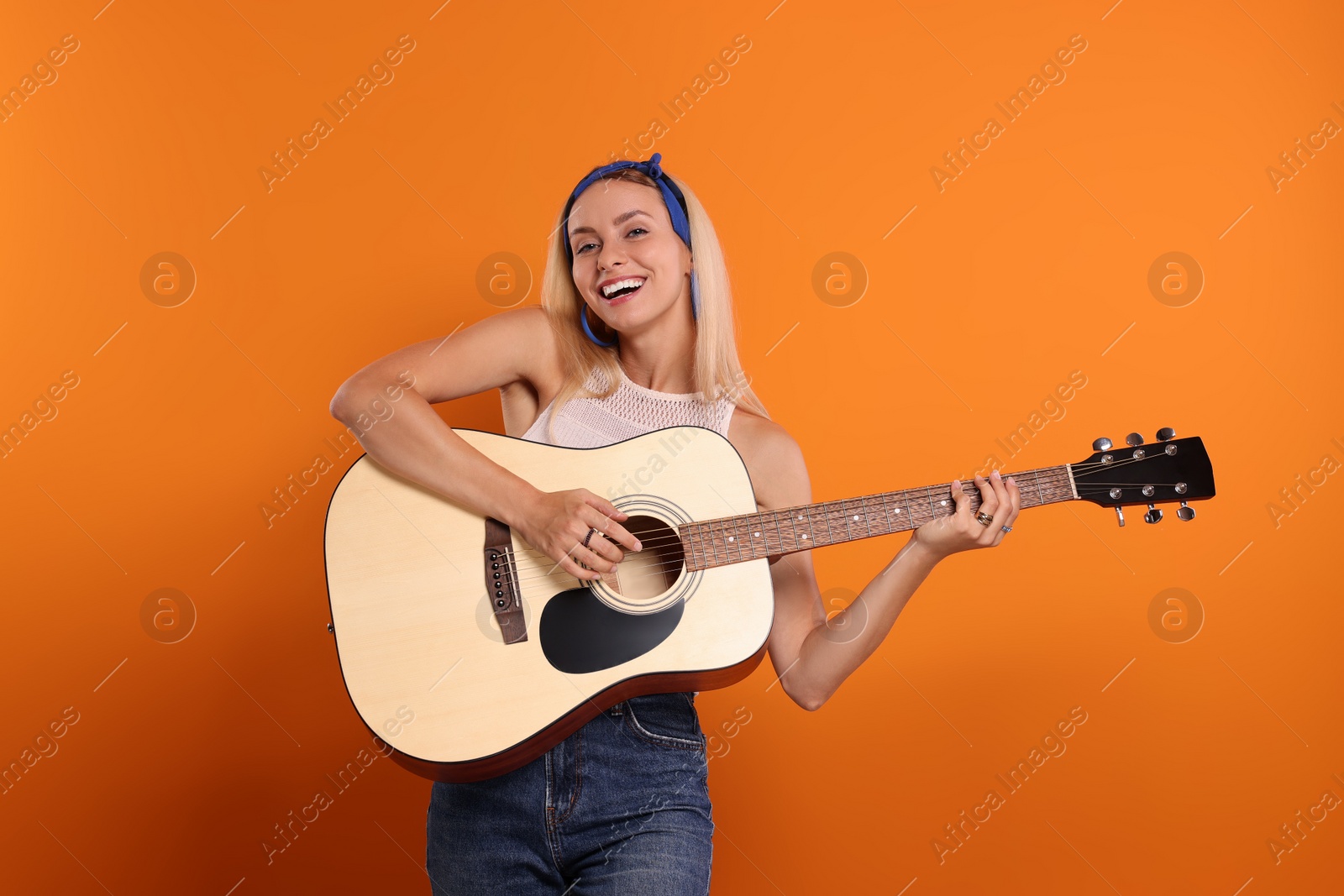 Photo of Happy hippie woman playing guitar on orange background