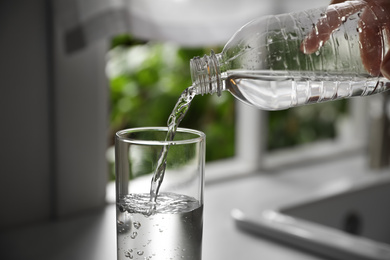Photo of Person pouring water from bottle into glass in kitchen, closeup