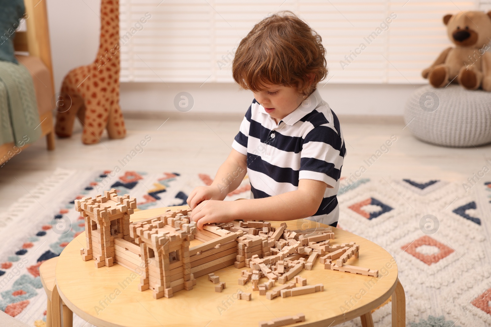 Photo of Cute little boy playing with wooden construction set at table in room. Child's toy