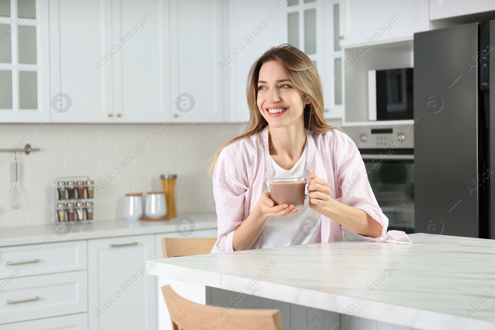 Photo of Young woman with glass cup of chocolate milk in kitchen