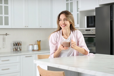 Young woman with glass cup of chocolate milk in kitchen