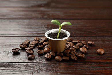 Photo of Coffee capsule with seedling and beans on wooden table, closeup
