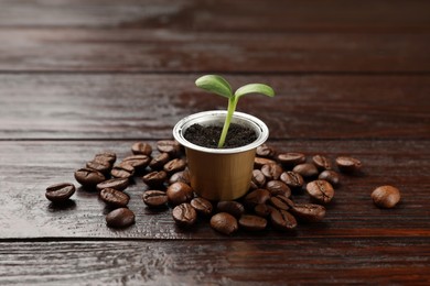 Coffee capsule with seedling and beans on wooden table, closeup