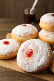 Many delicious donuts with jelly and powdered sugar on wooden table, closeup