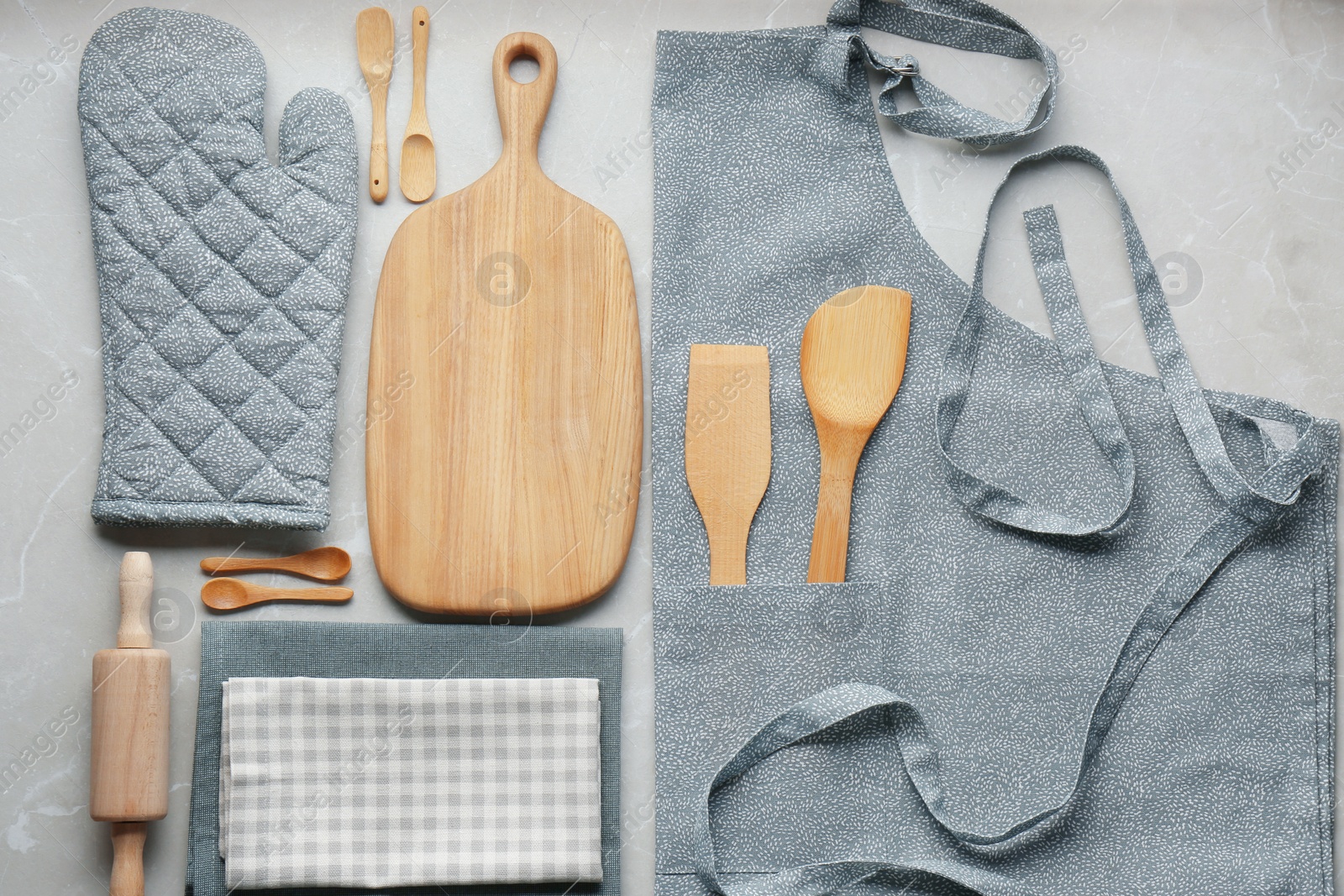 Photo of Kitchen napkins, apron and different utensils on light grey table, flat lay