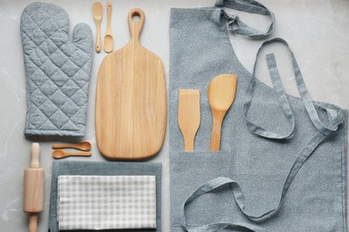 Kitchen napkins, apron and different utensils on light grey table, flat lay