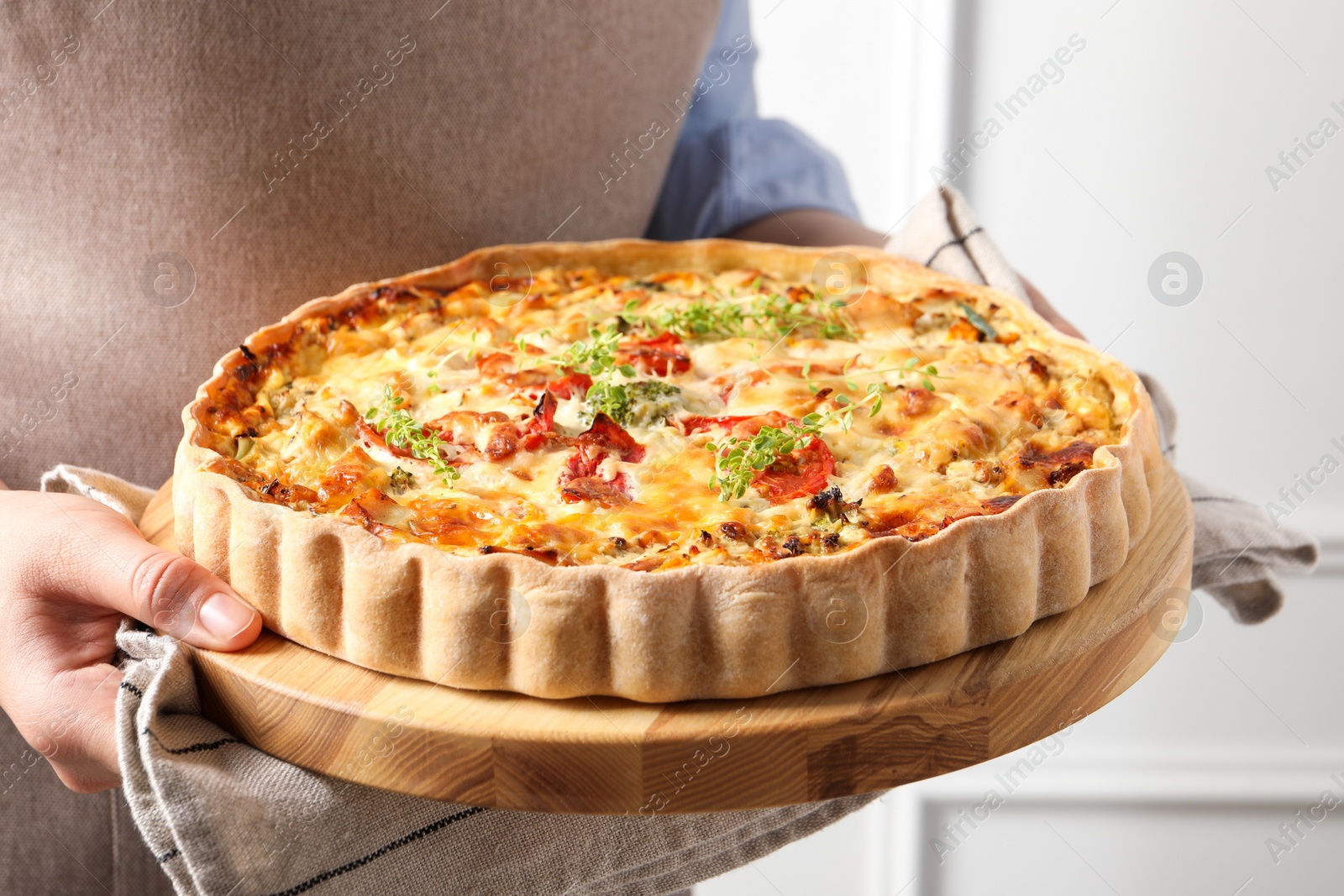 Photo of Woman holding board with tasty quiche indoors, closeup