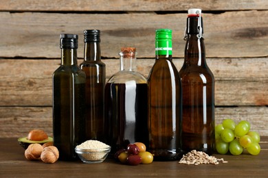 Photo of Vegetable fats. Different cooking oils in glass bottles and ingredients on wooden table