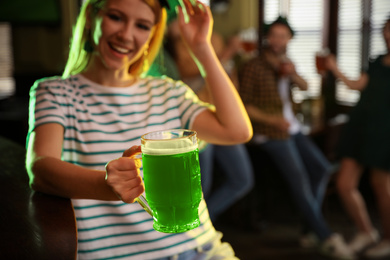 Photo of Young woman with glass of green beer in pub, focus on hand. St. Patrick's Day celebration