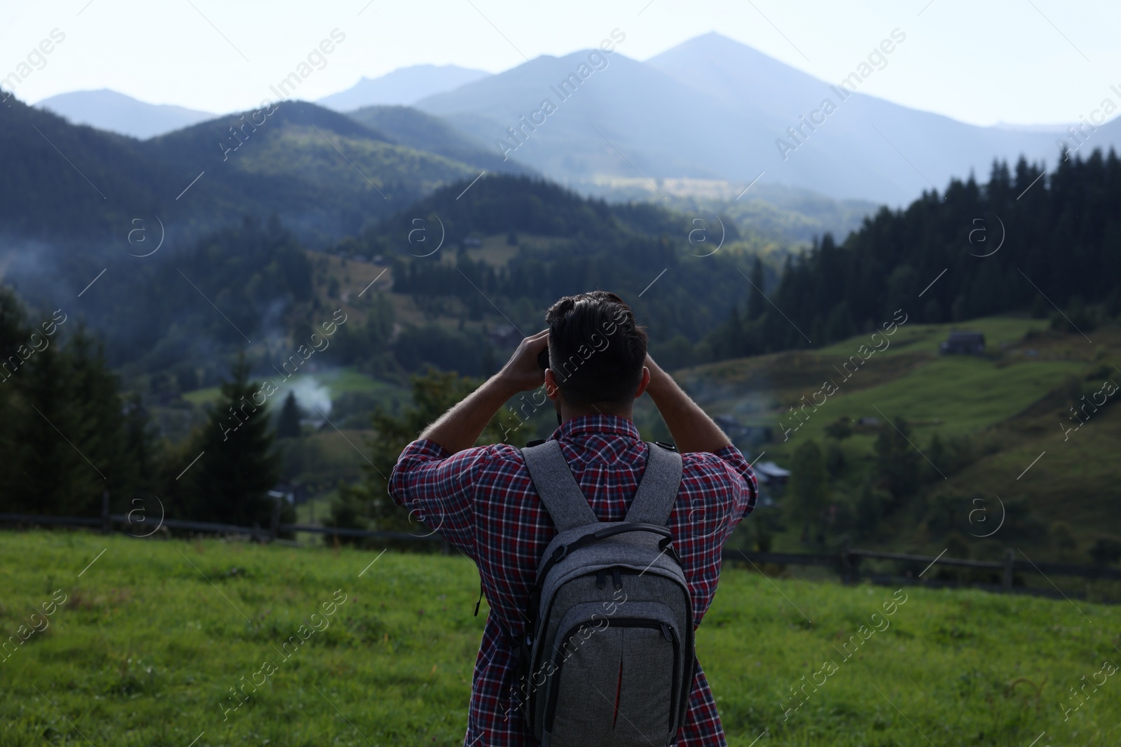 Photo of Tourist with backpack and binoculars enjoying landscape in mountains, back view