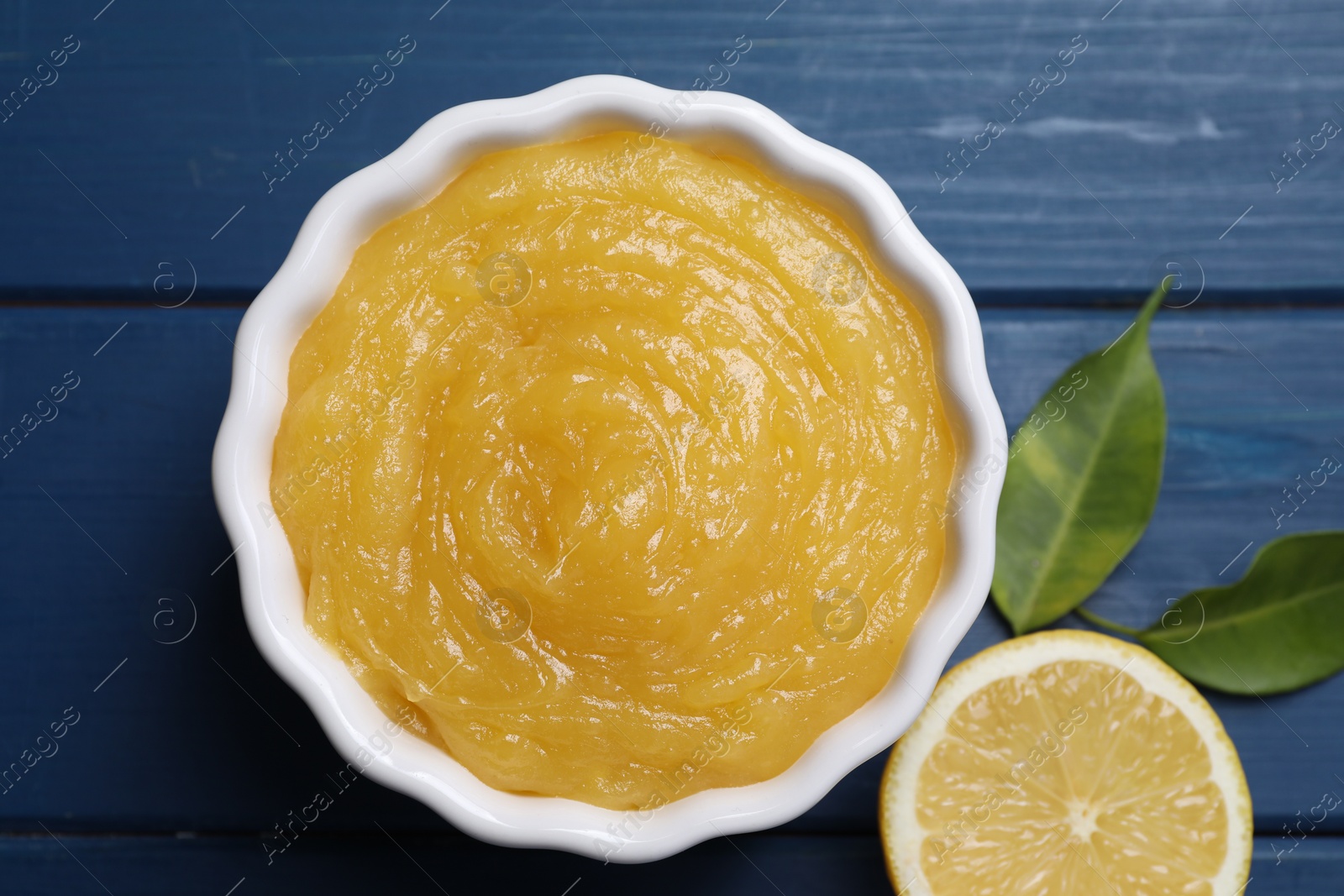 Photo of Delicious lemon curd in bowl and citrus fruit on blue wooden table, flat lay