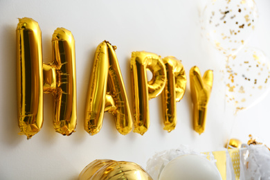 Word HAPPY made of golden balloon letters on white wall