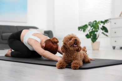 Photo of Young woman practicing yoga on mat with her cute dog at home, selective focus