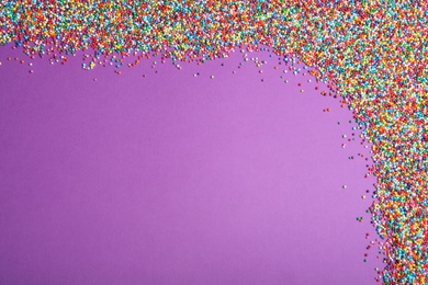 Photo of Colorful sprinkles on purple background, flat lay with space for text. Confectionery decor