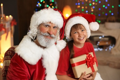 Photo of Little child with Santa Claus and Christmas gift at home