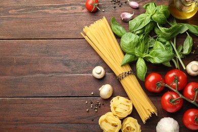 Different types of pasta, spices and products on wooden table, flat lay. Space for text