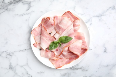 Photo of Plate of sliced raw bacon on white marble table, top view