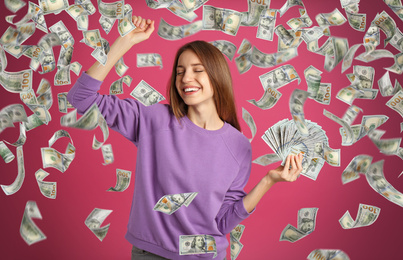 Happy young woman with dollars under money rain on pink background