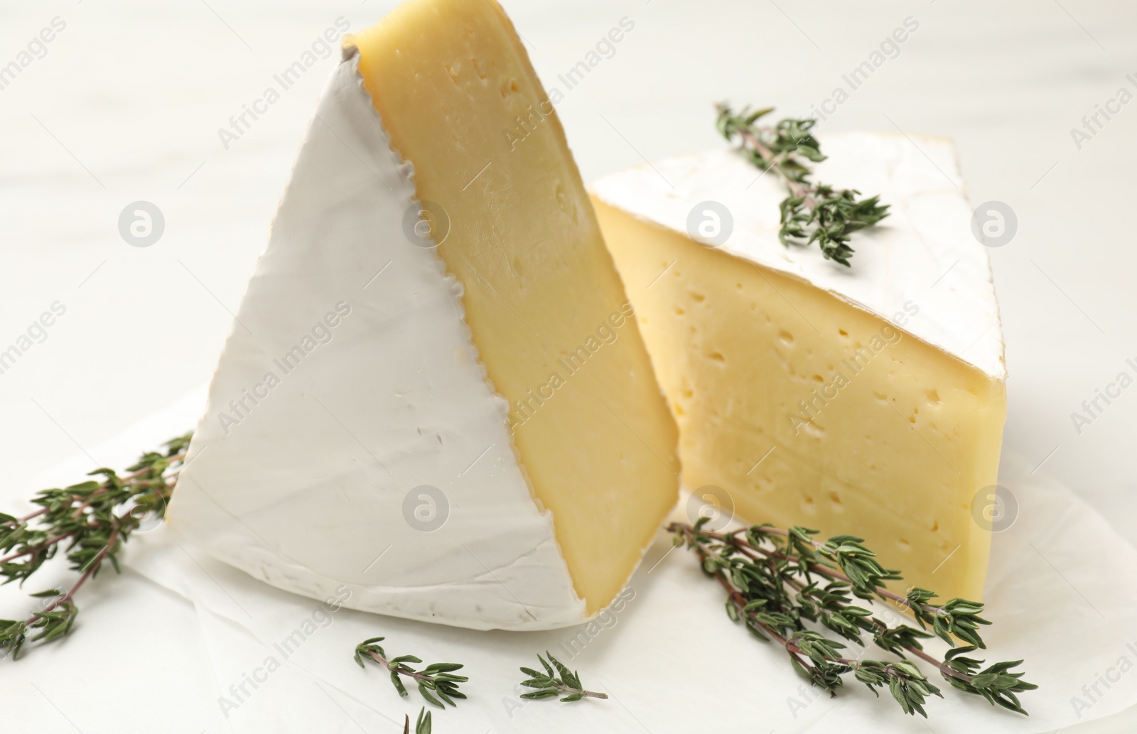 Photo of Pieces of tasty camembert cheese and thyme on white table, closeup