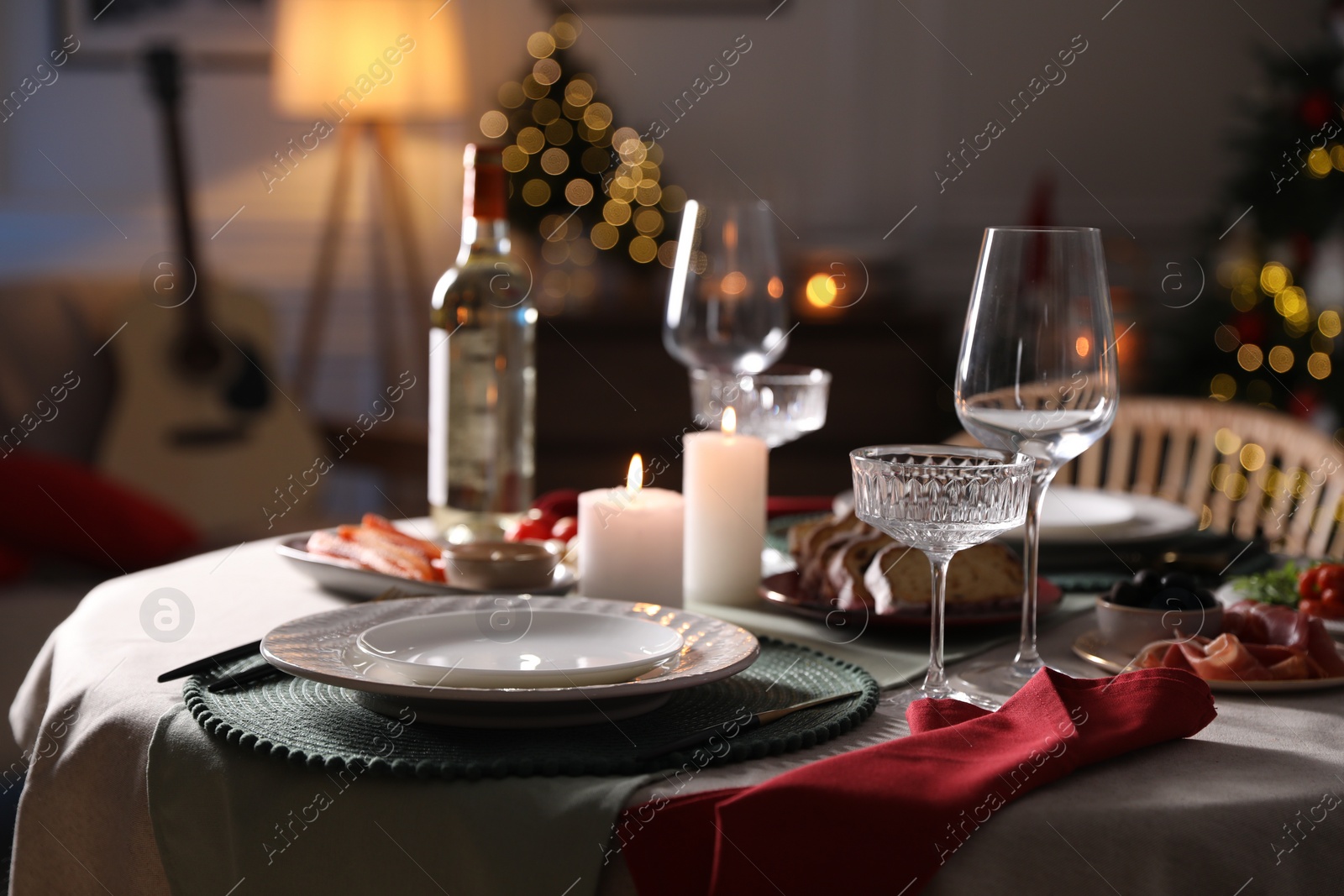 Photo of Christmas table setting with burning candles, appetizers and dishware indoors