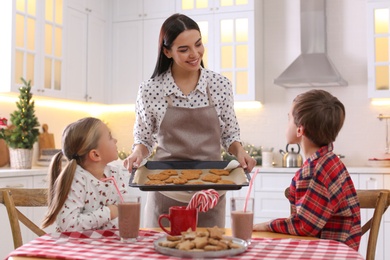 Photo of Mother giving her cute little children freshly baked Christmas cookies in kitchen