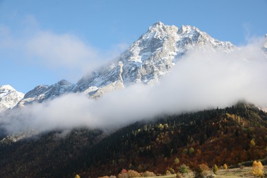 Picturesque landscape of high mountains covered with thick mist under blue sky on autumn day