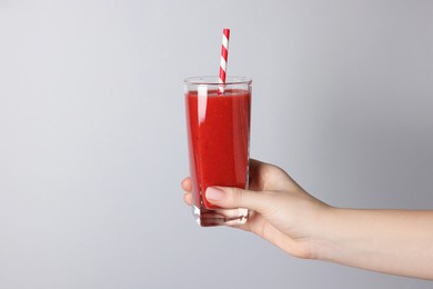 Photo of Woman holding glass of tasty smoothie on light grey background, closeup