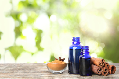 Image of Bottles of essential oil, cinnamon sticks and powder on wooden table against blurred background. Space for text