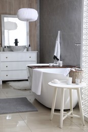 Photo of Modern white tub and table with toiletries in bathroom. Interior design