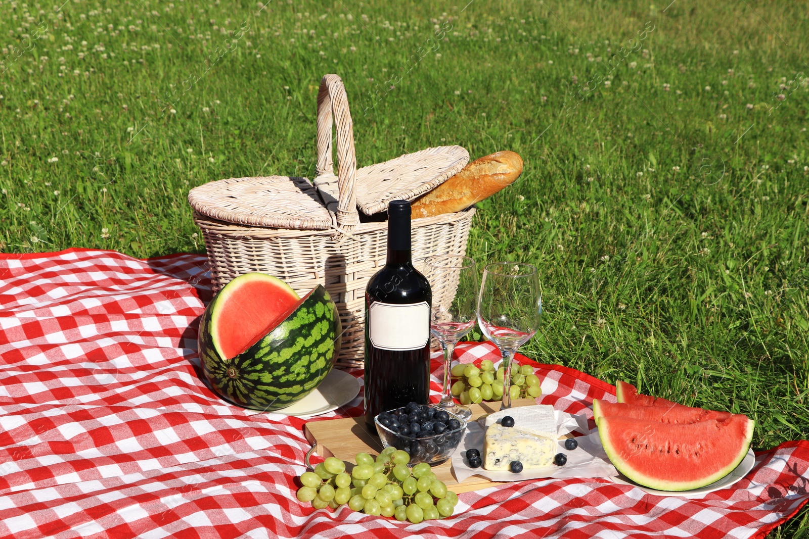 Photo of Picnic blanket with delicious food and wine outdoors on summer day