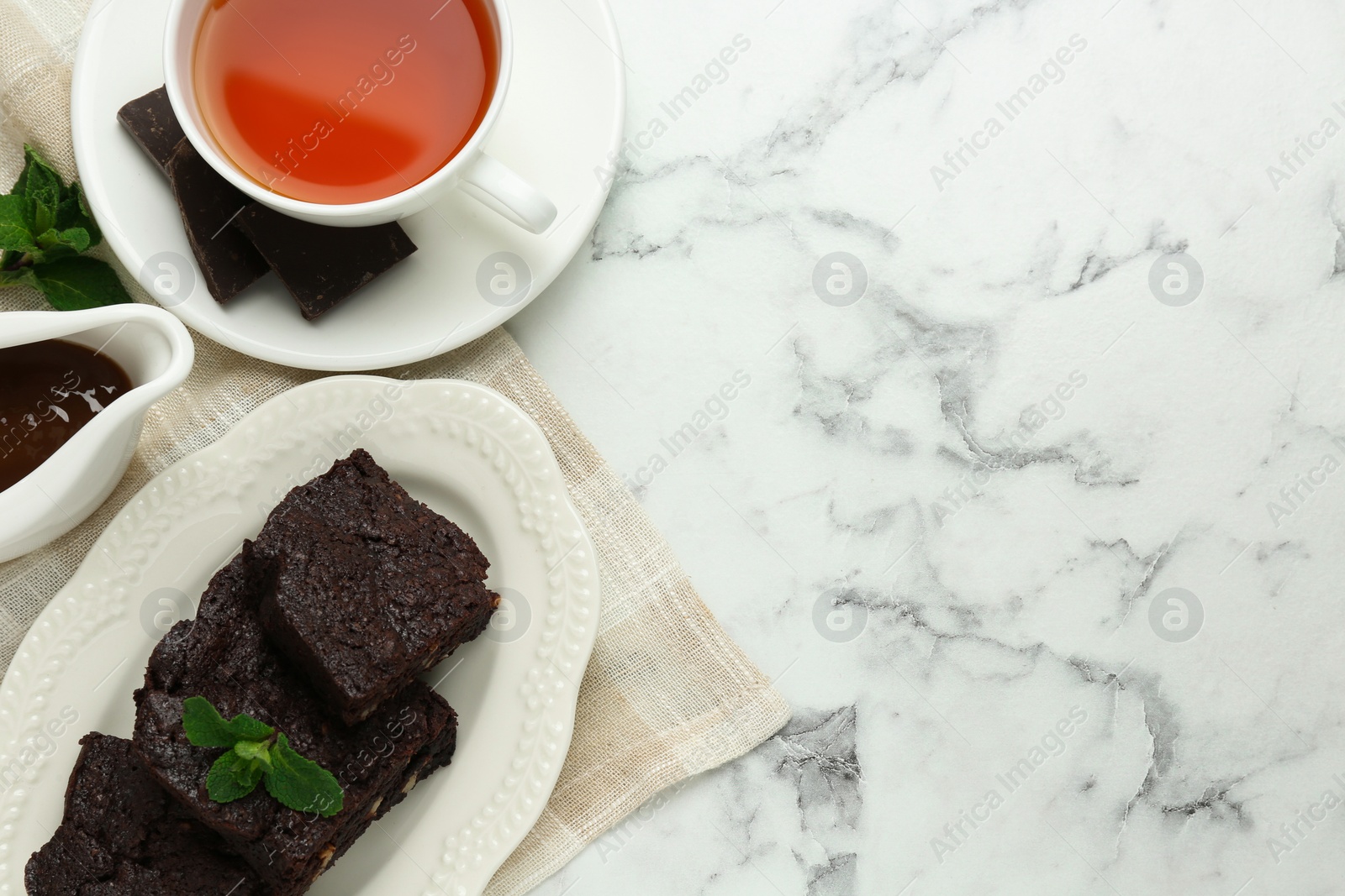 Photo of Delicious brownies served with tea and chocolate syrup on white marble table, flat lay. Space for text