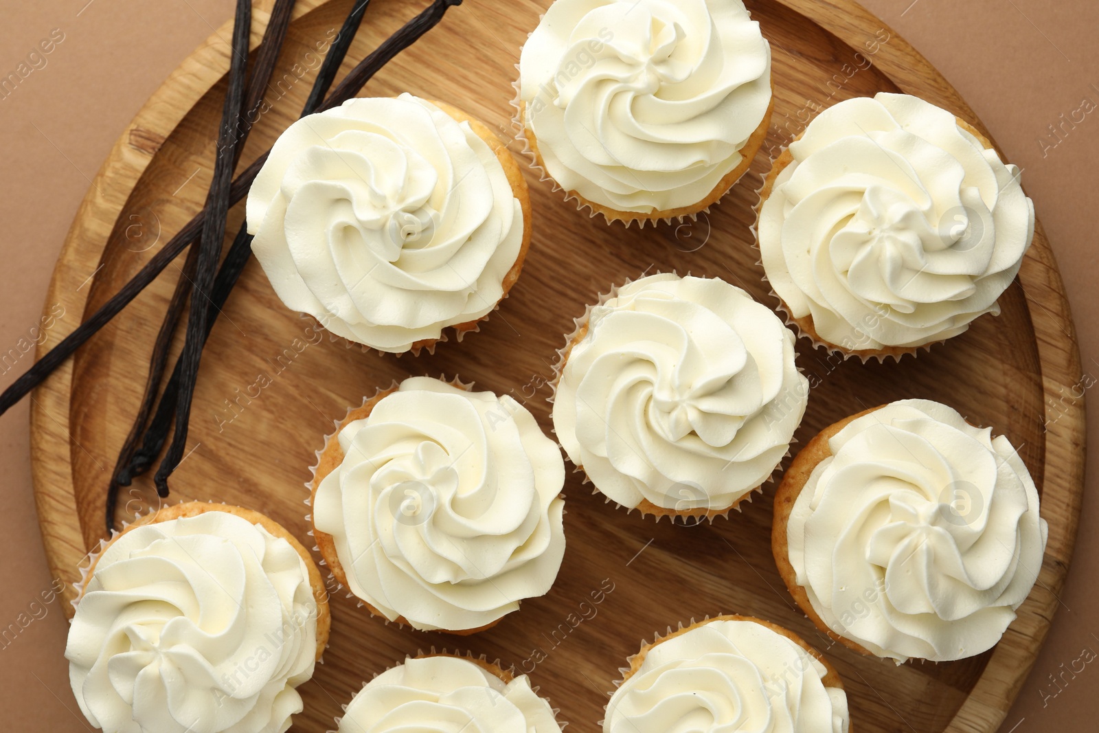 Photo of Tasty cupcakes with cream and vanilla pods on dark beige background, top view