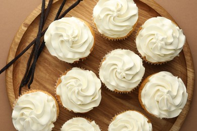 Tasty cupcakes with cream and vanilla pods on dark beige background, top view