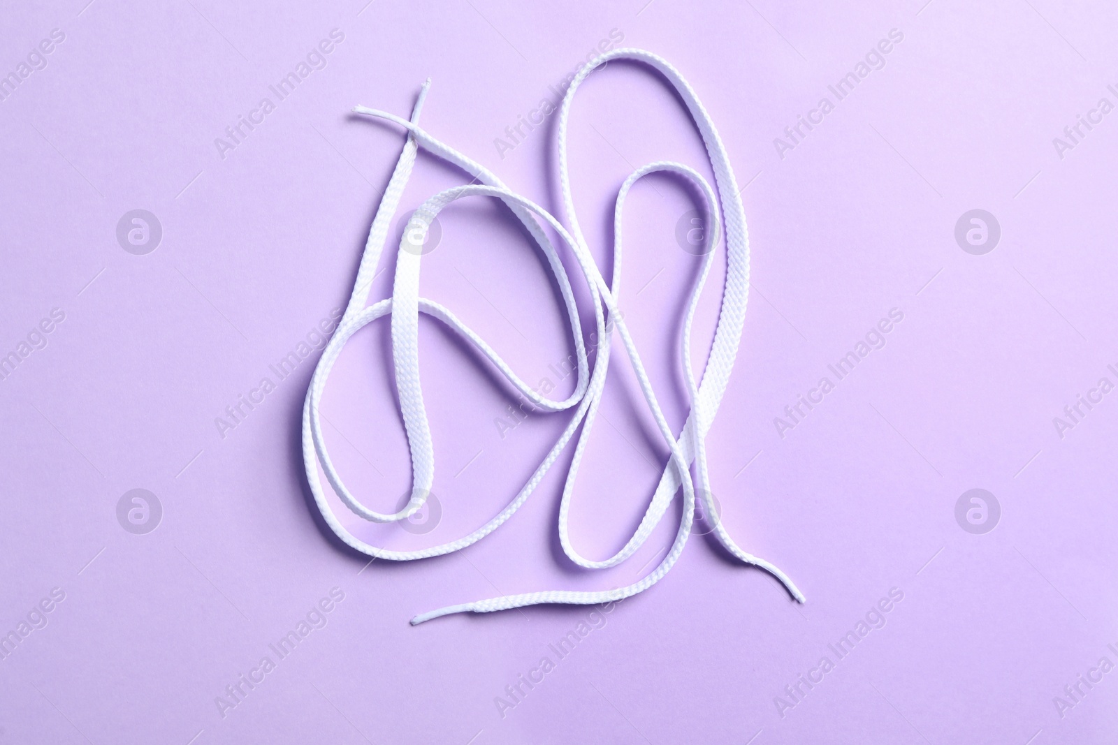 Photo of White shoelaces on lilac background, flat lay