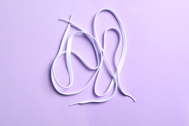 White shoelaces on lilac background, flat lay