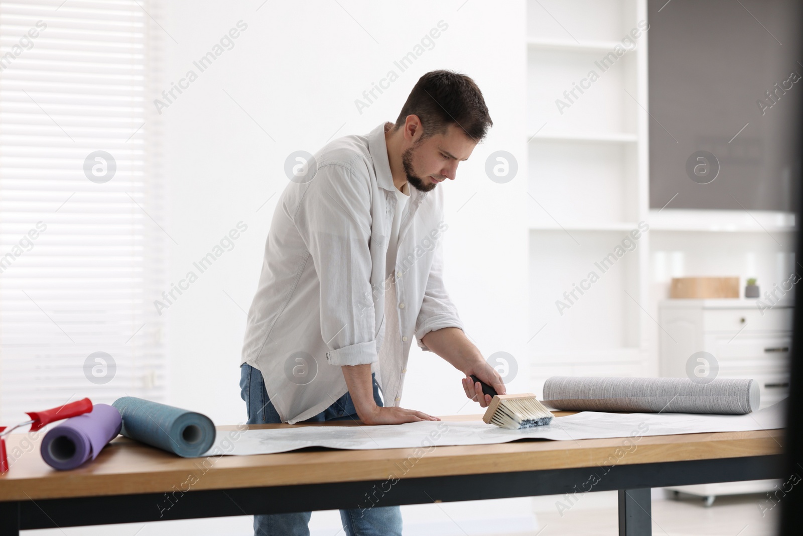 Photo of Man applying glue onto wallpaper sheet at wooden table indoors